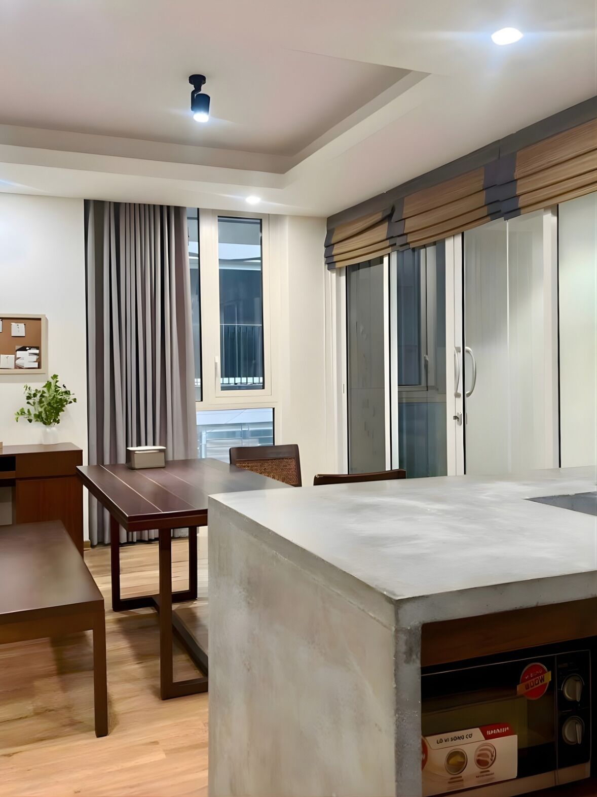 A modern kitchen with a built-in microwave, wooden dining table, and a large window with curtains.