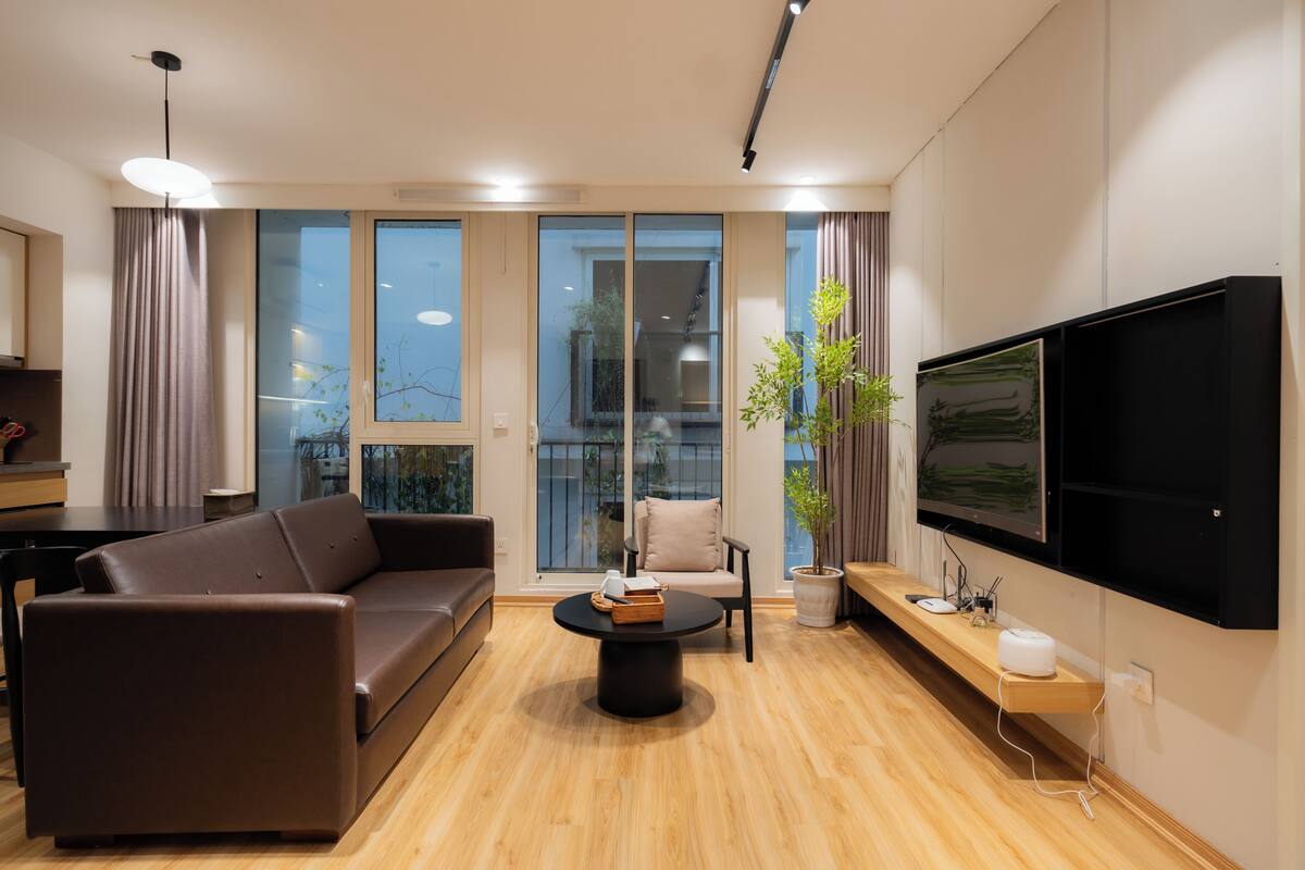 Un salon moderne avec un canapé en cuir marron, une table basse ronde, une plante en pot, un téléviseur à écran plat fixé au mur et un plancher en bois.