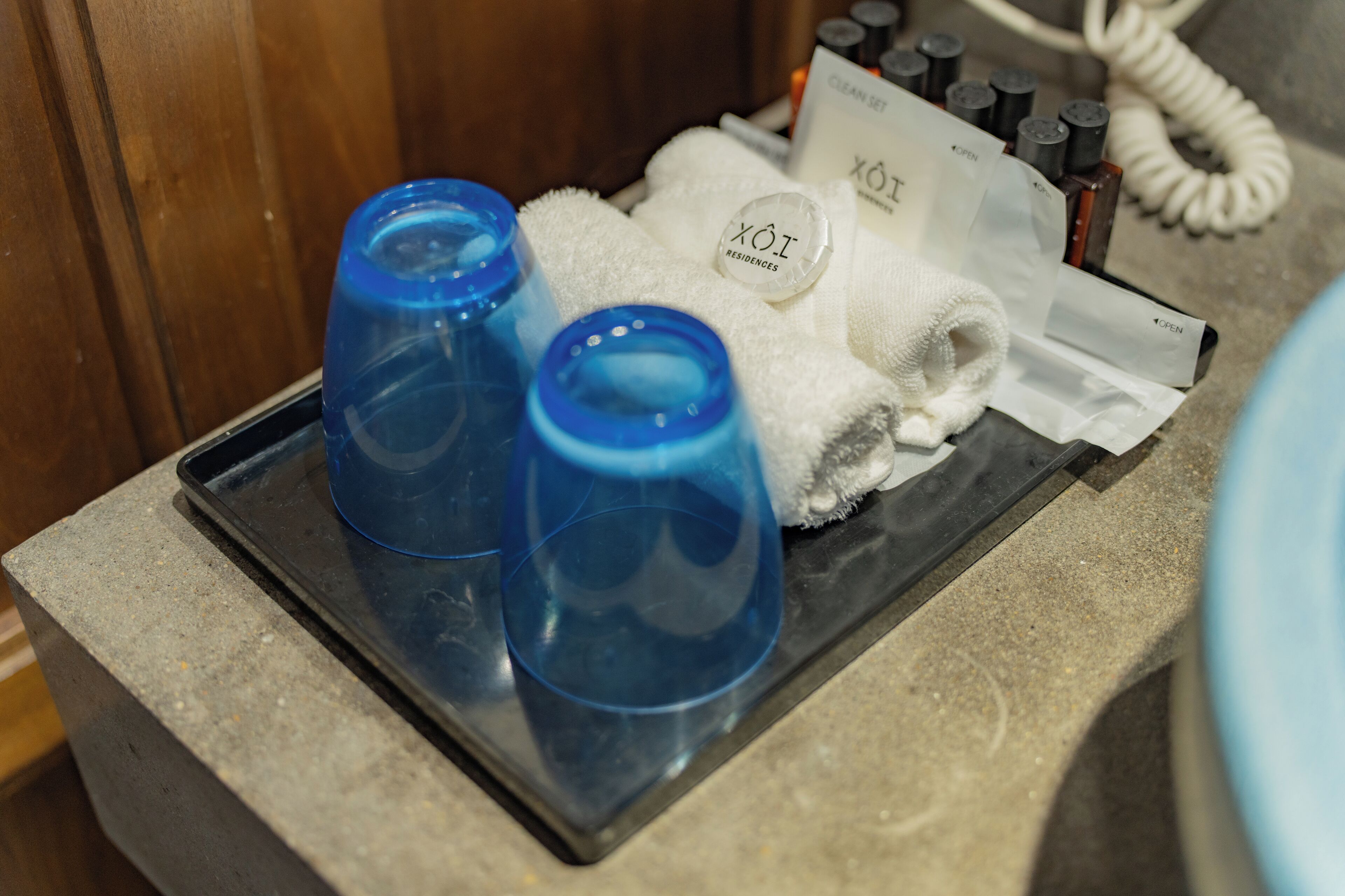 Un plateau contenant deux verres bleus, une serviette blanche et une carte portant l’inscription « XÔI RESIDENCES », le tout posé sur un comptoir en pierre.