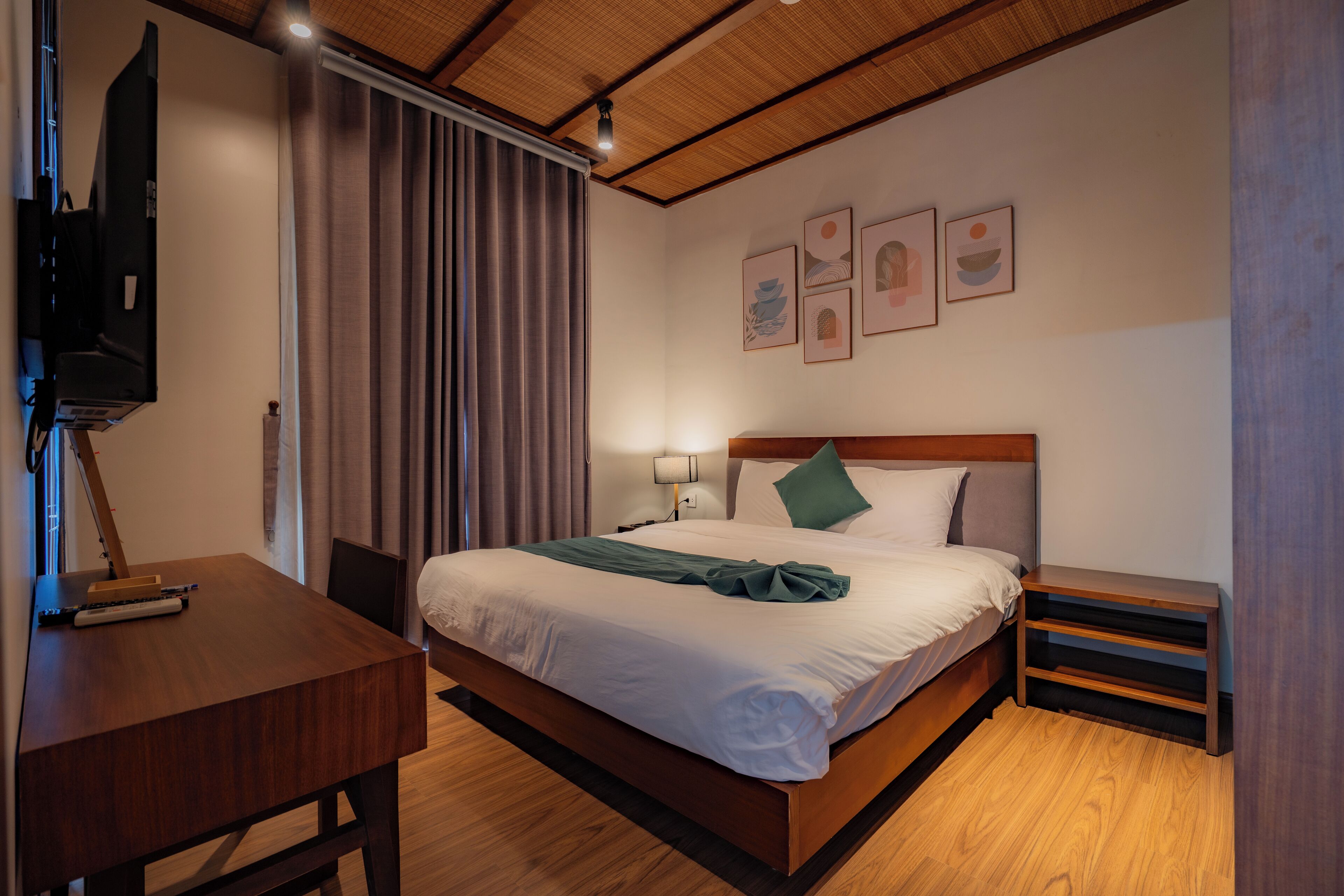 A neatly arranged hotel room with a bed, bedside table, lamp, and a flat-screen TV mounted on the wall.