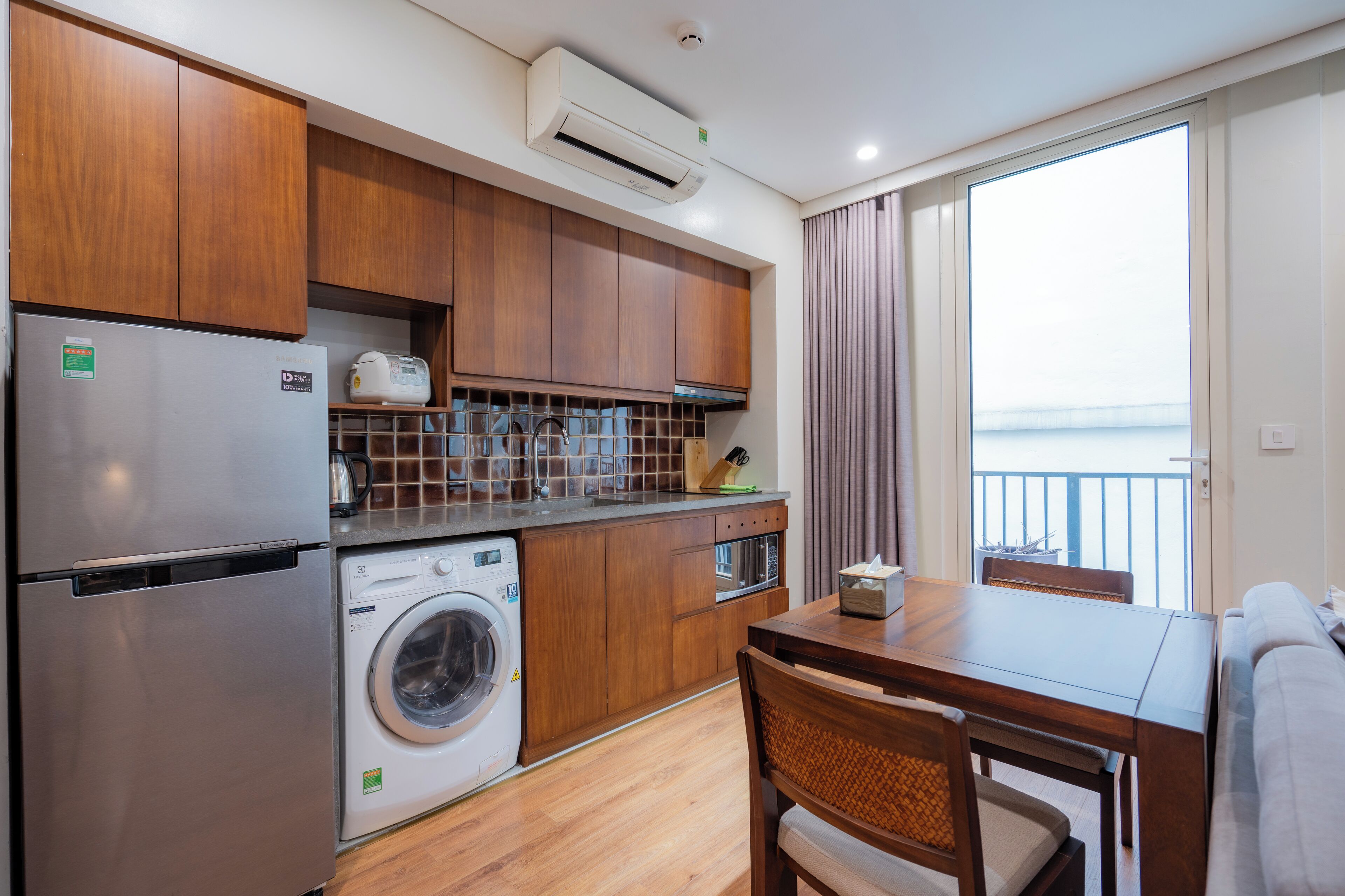A compact kitchen with wooden cabinets, a washing machine, a built-in oven, and a dining area with a table and chairs.