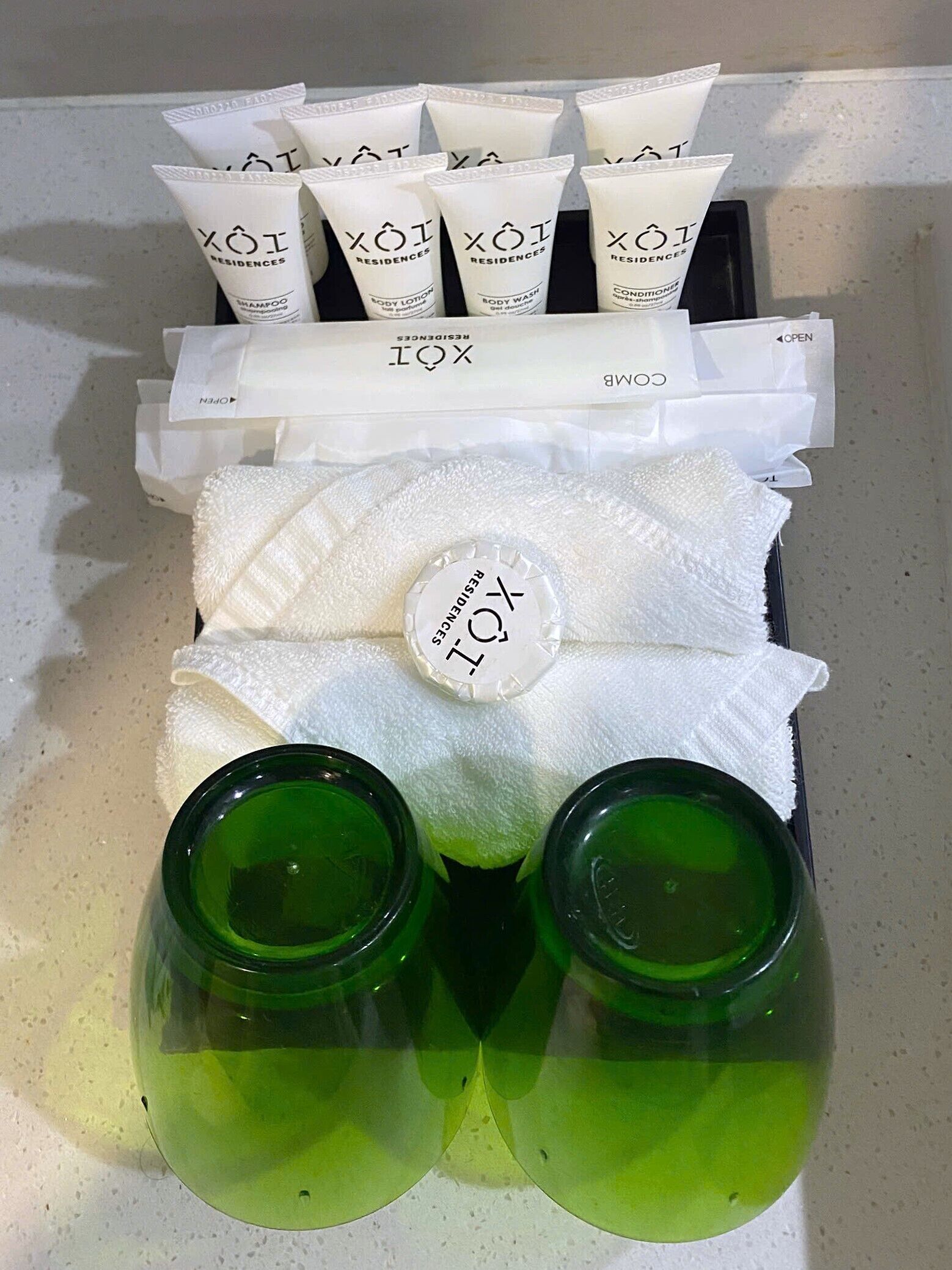 Un conjunto de artículos de aseo que incluye champú, loción corporal, gel de ducha y acondicionador, junto con una toalla y dos botellas verdes, probablemente con champú o acondicionador.
