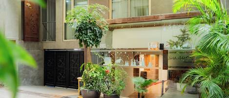 Entrada de un hotel con una planta grande en maceta, una puerta metálica y un letrero sobre la entrada.