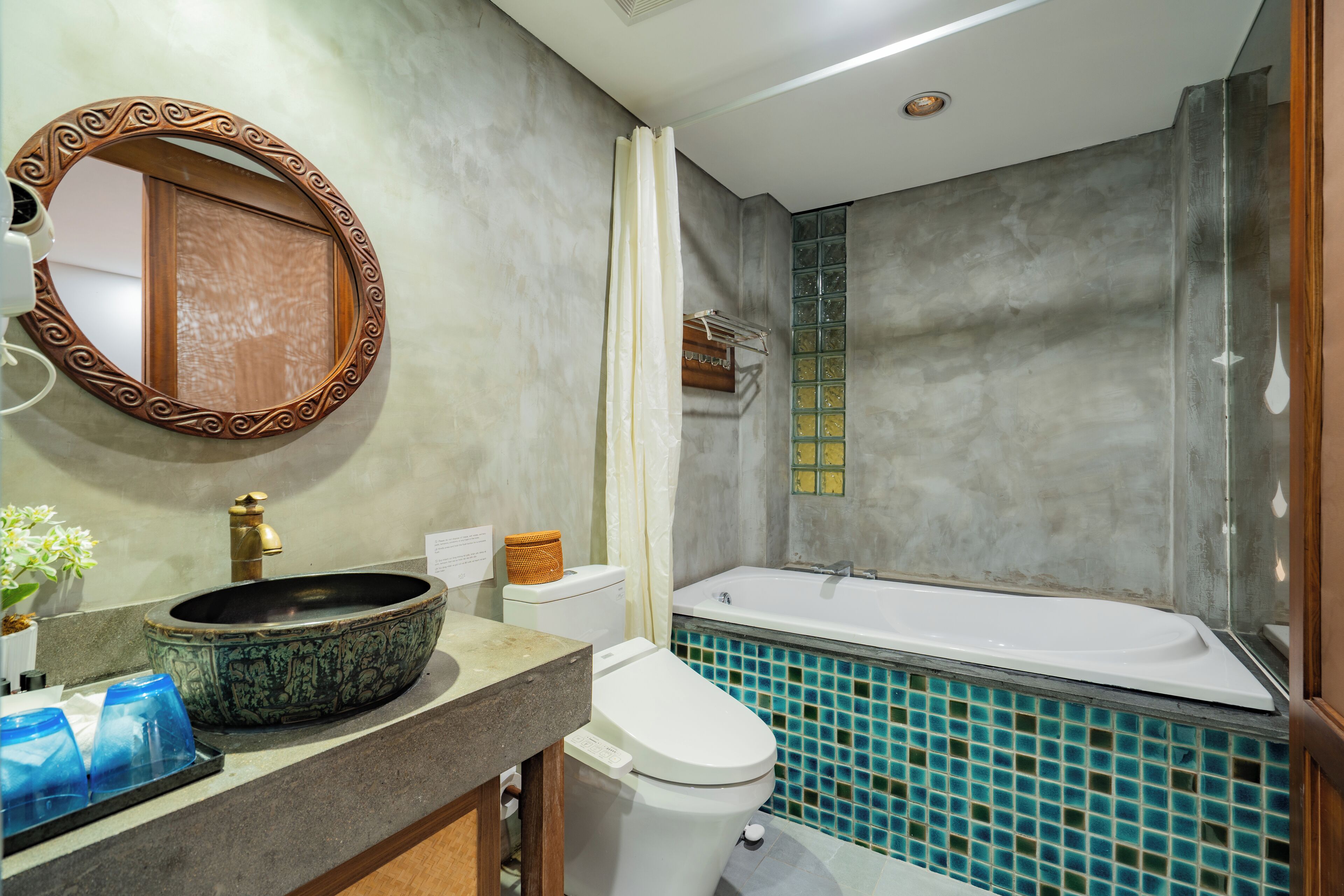 A bathroom with a round mirror, a sink, a toilet, and a bathtub with blue mosaic tiles.