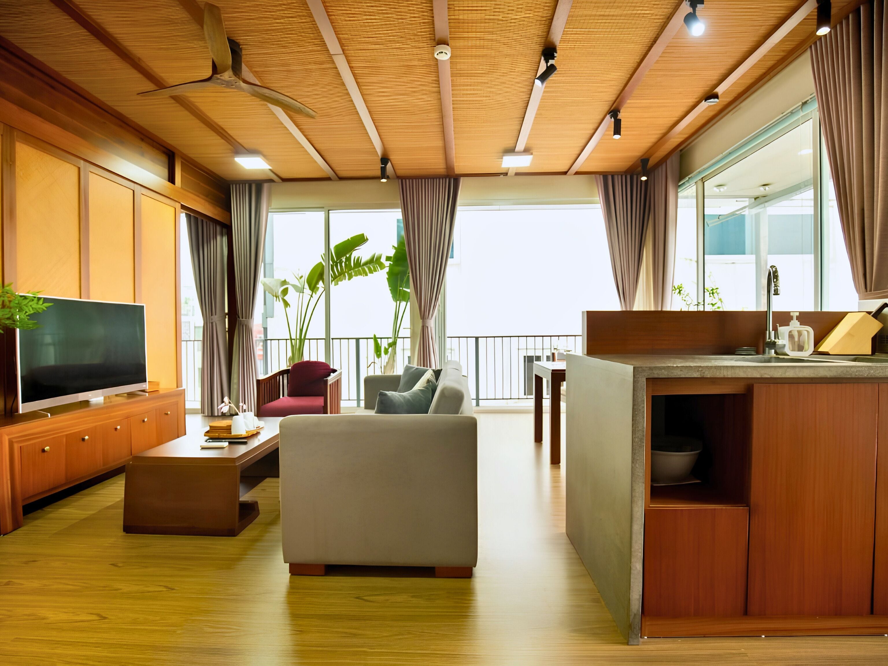 A modern living room with a flat-screen TV, a sofa, a dining area, and a kitchen counter.