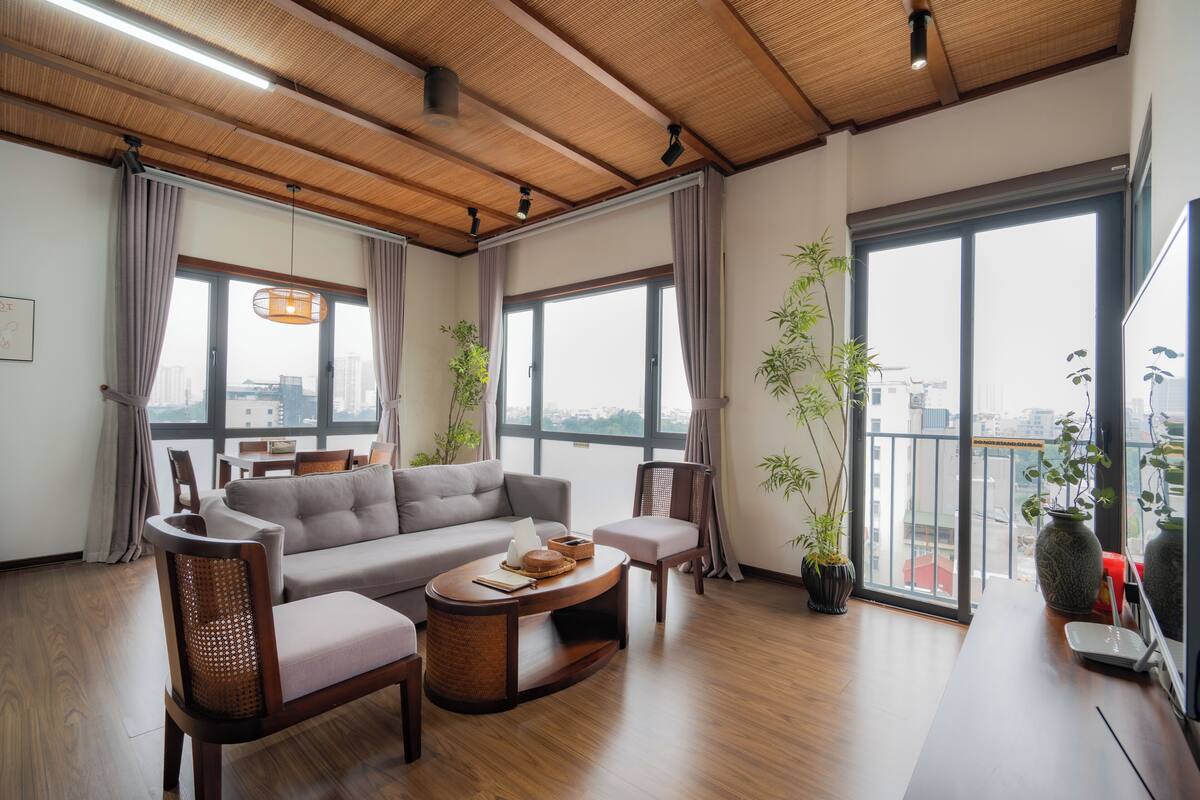 Un salon moderne avec un plafond en bois, de grandes fenêtres, un canapé, des fauteuils, une table basse et des plantes en pot.
