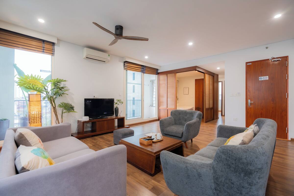 Un salon moderne comprenant un canapé, des fauteuils, une table basse, un téléviseur et un ventilateur de plafond.