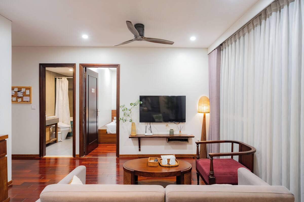 Une chambre d’hôtel moderne équipée d’un téléviseur à écran plat, d’un ventilateur de plafond, d’une table basse en bois et d’un canapé.