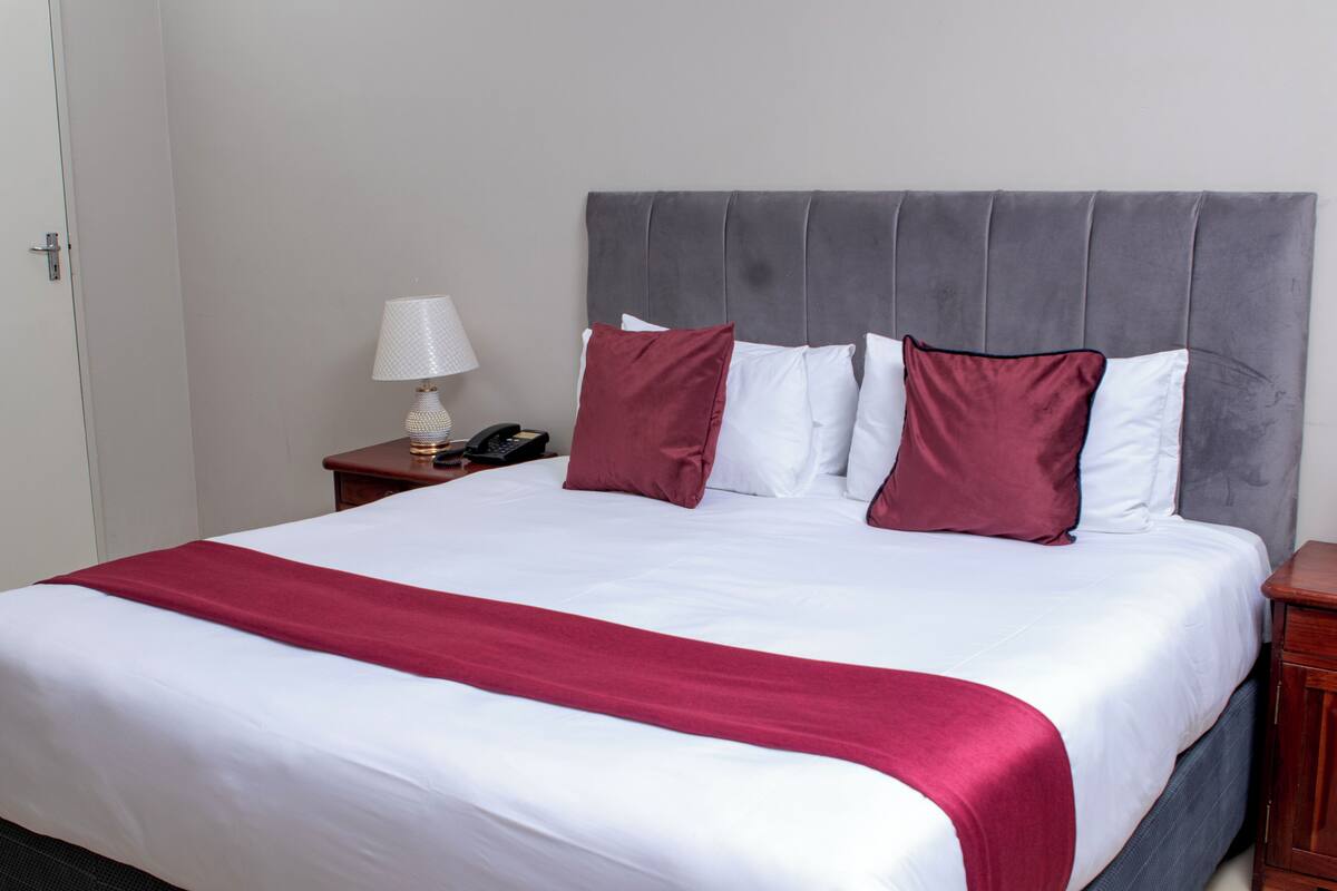 A neatly made bed with a grey upholstered headboard, white bedding, and a red accent throw.