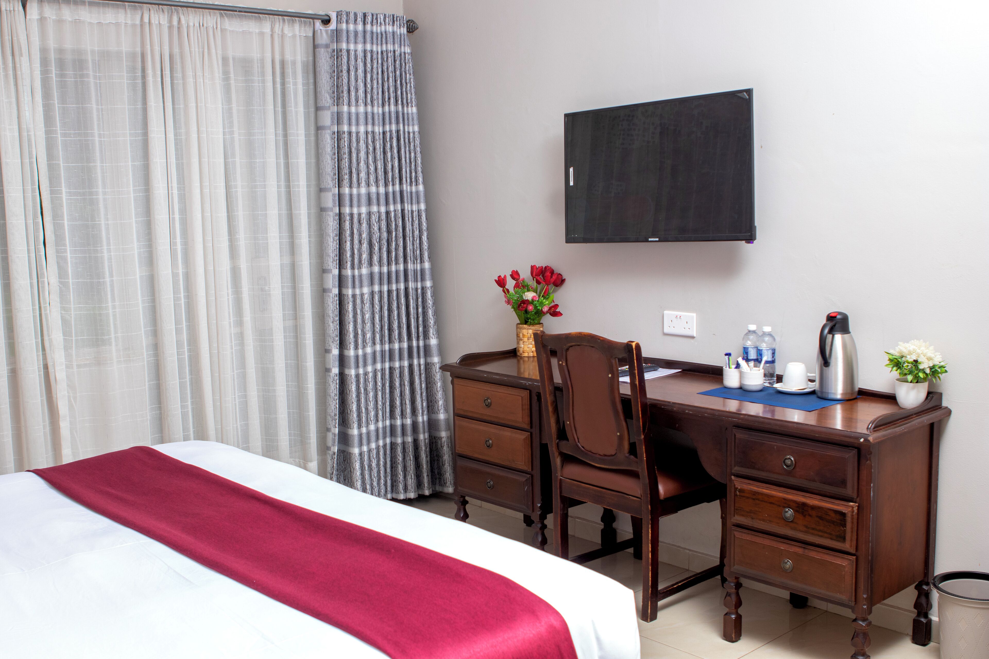 A hotel room with a bed, a desk with a chair, a television, and a small table with a vase of flowers.
