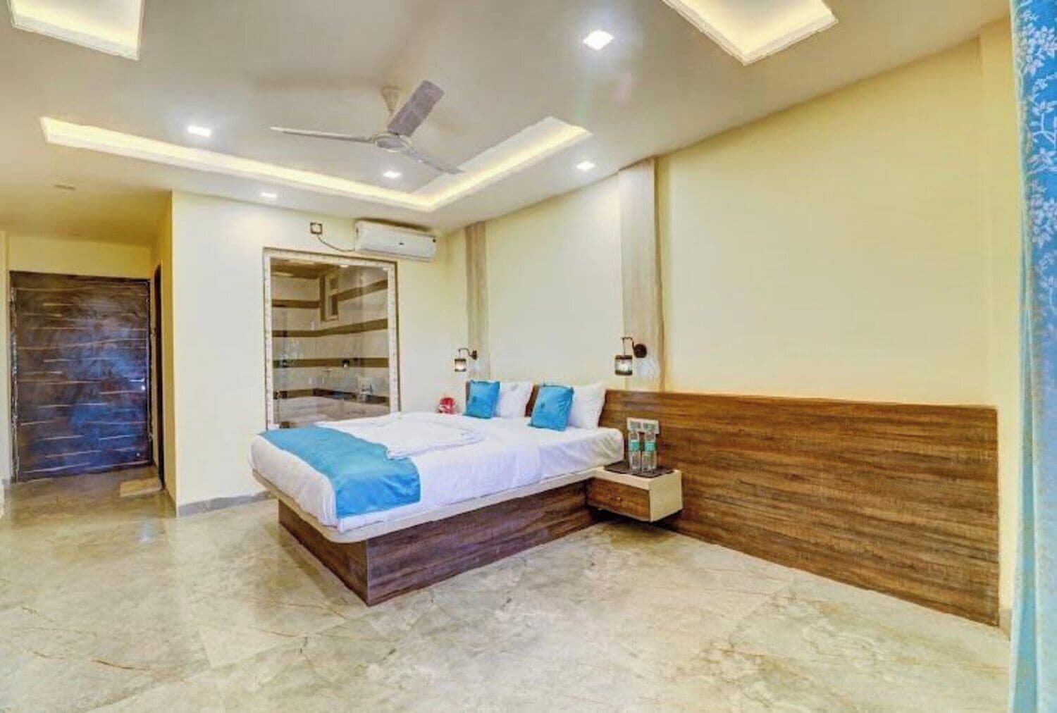 Ein modernes Hotelzimmer mit einem großen Bett, einem Deckenventilator, Einbaustrahlern und einem Holz-Kopfstück.
