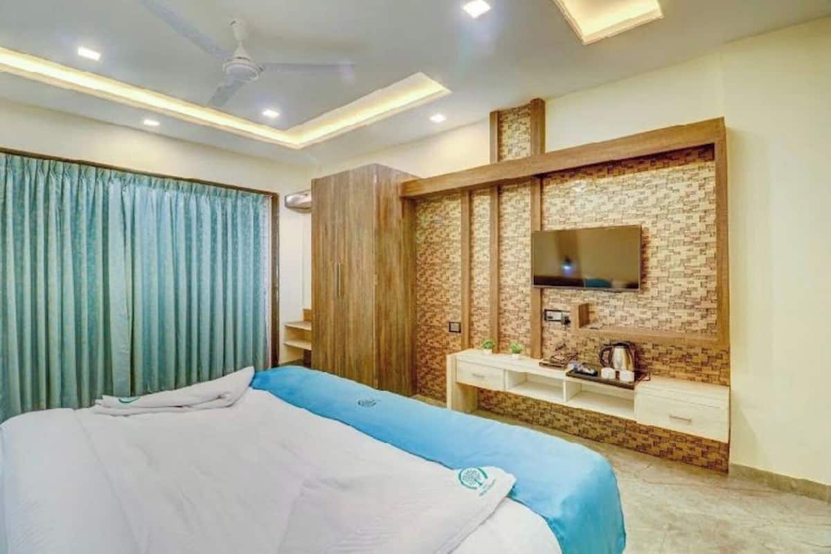 A hotel room with a bed, a TV mounted on a brick-patterned wall, a bedside table, and a wardrobe.