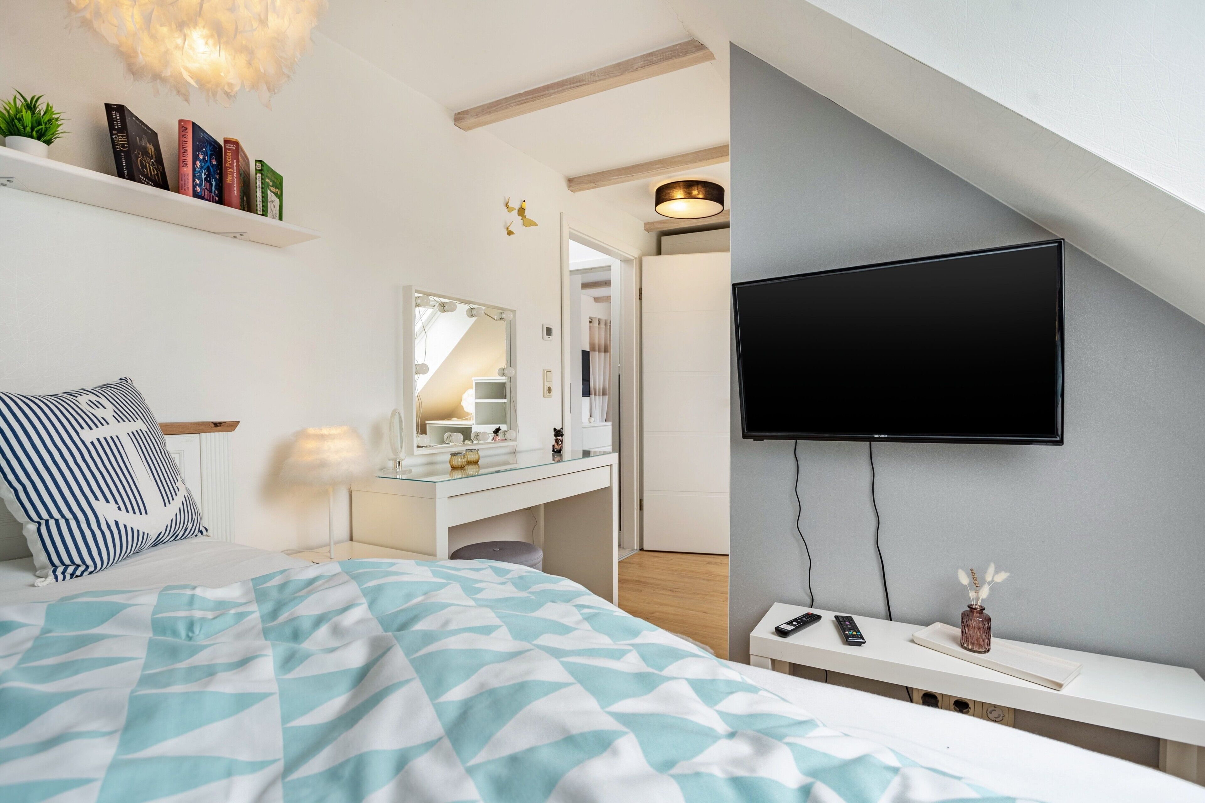A modern bedroom with a bed, bedside table, TV, and a vanity with a mirror.