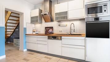 A modern kitchen with white cabinetry, stainless steel appliances, a dishwasher, and a wooden staircase.