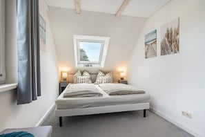 Ein Schlafzimmer mit einem Bett, einem Dachfenster, einem Nachttisch und zwei Wandlampen.