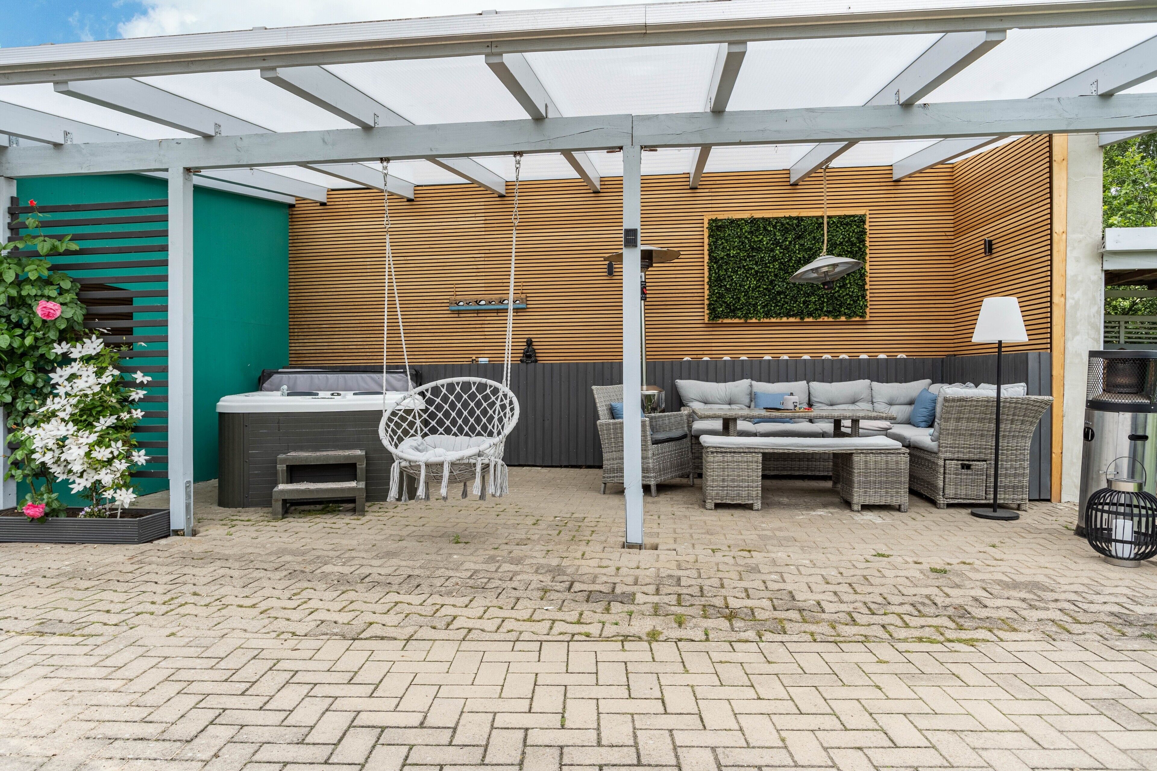 Een terras buiten met een houten muur, een hangstoel, een zithoek en een tafel.
