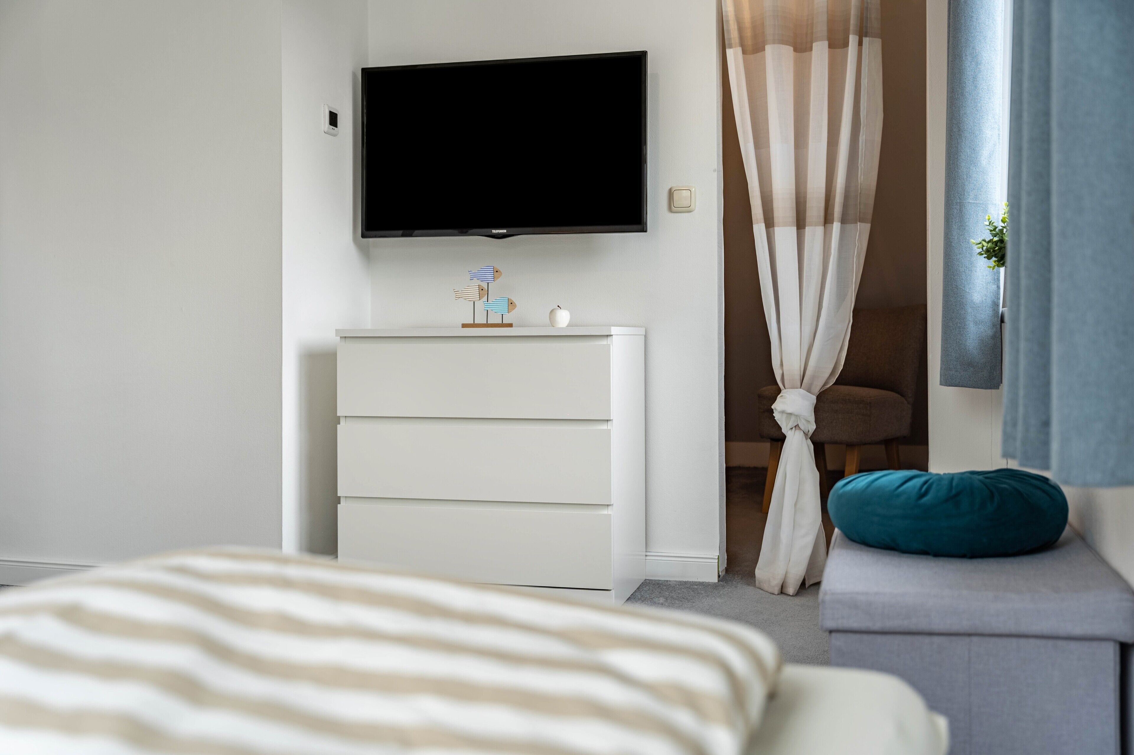Een slaapkamer met een bed, een dressoir, een televisie en een raam met gordijnen.