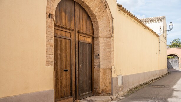 A narrow street with a large wooden door and a brick archway.