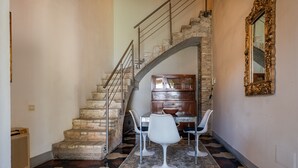 A staircase with a stone wall, a dining area with a table and chairs, and a mirror on the wall.