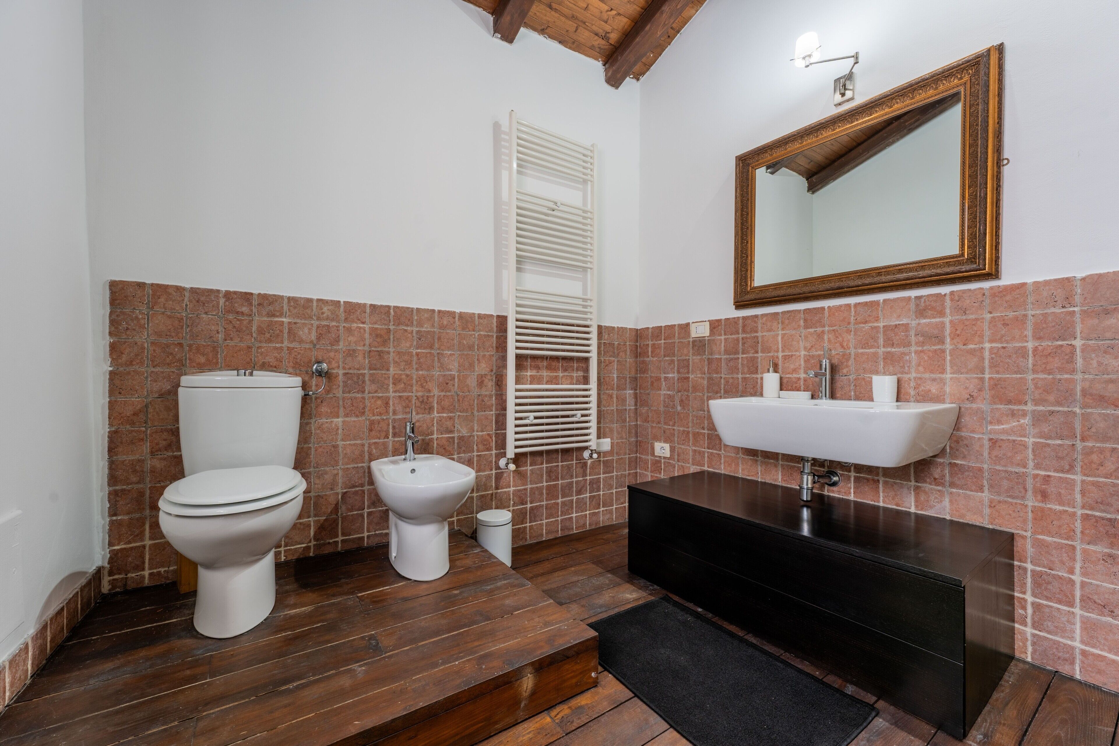 Une salle de bain comprenant des toilettes, un bidet, un lavabo, un miroir et un porte-serviettes.