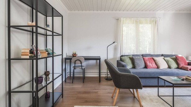 A modern living room with a bookshelf, a desk, a grey sofa with cushions, and a coffee table. - Cozy and Stylish Apartment in Norberg (Norberg)