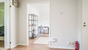 A hallway with a white door, a metal shelf unit, a small table with chairs, and a fire extinguisher. - Cozy and Stylish Apartment in Norberg (Norberg)