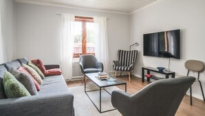 A living room with a sofa, armchairs, a coffee table, a TV, and a window with curtains. - Cozy and Stylish Apartment in Norberg (Norberg)