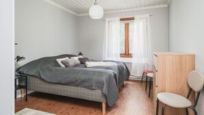 A bedroom with a bed, a desk, a chair, a window with curtains, and a hanging light fixture. - Cozy and Stylish Apartment in Norberg (Norberg)