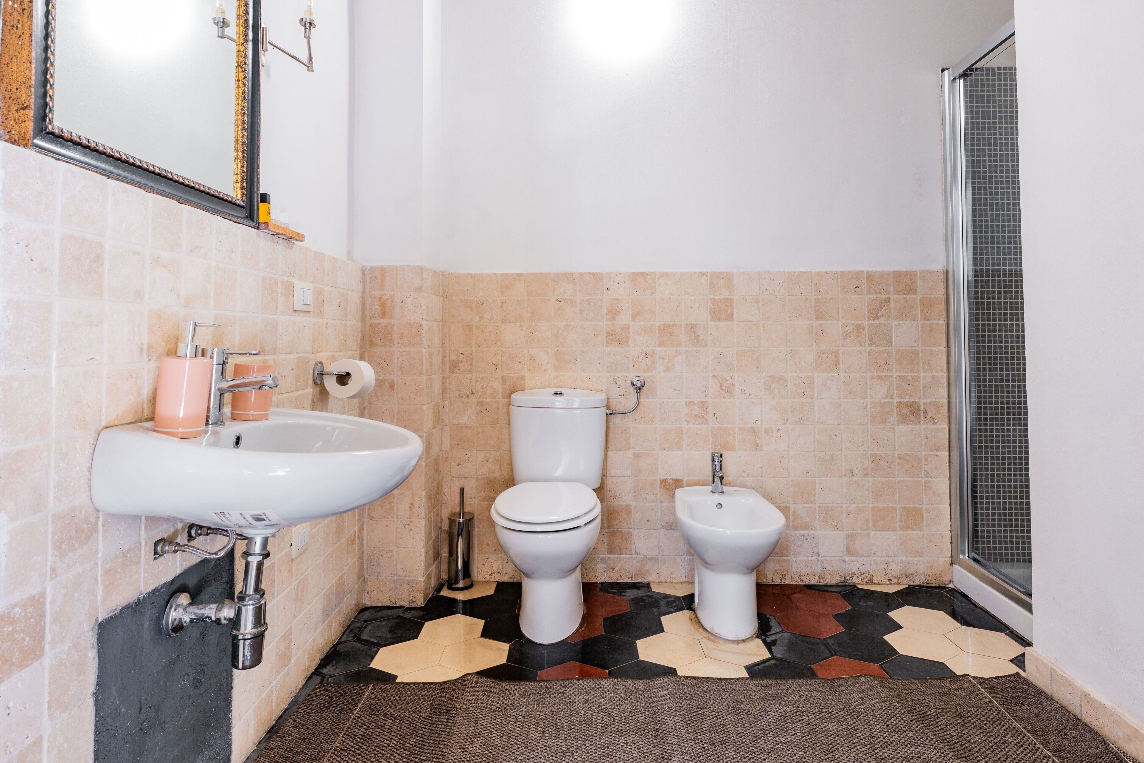 A bathroom with a sink, two toilets, a shower, and a patterned floor.