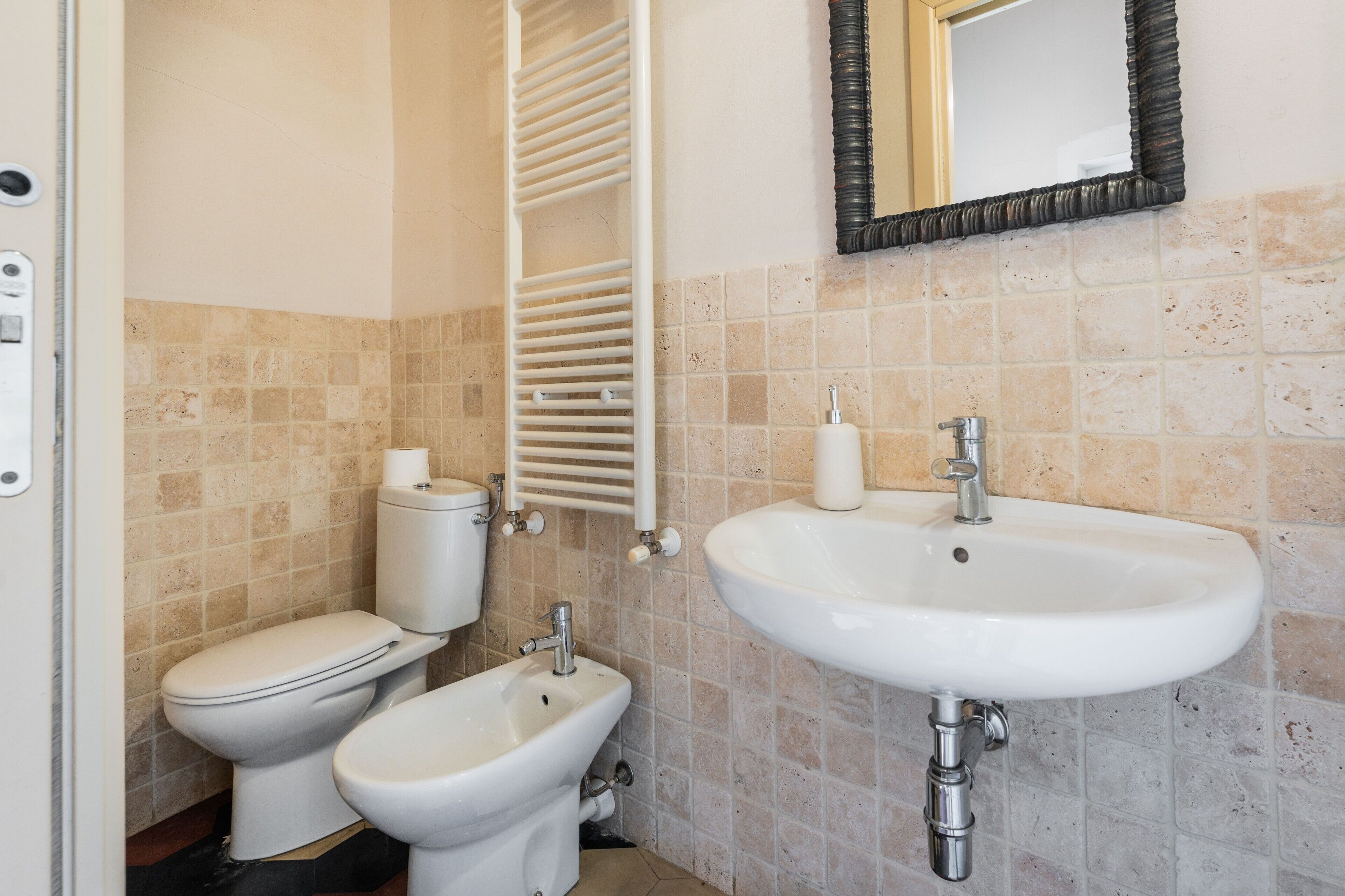 A bathroom with a toilet, bidet, sink, towel rack, and a mirror.