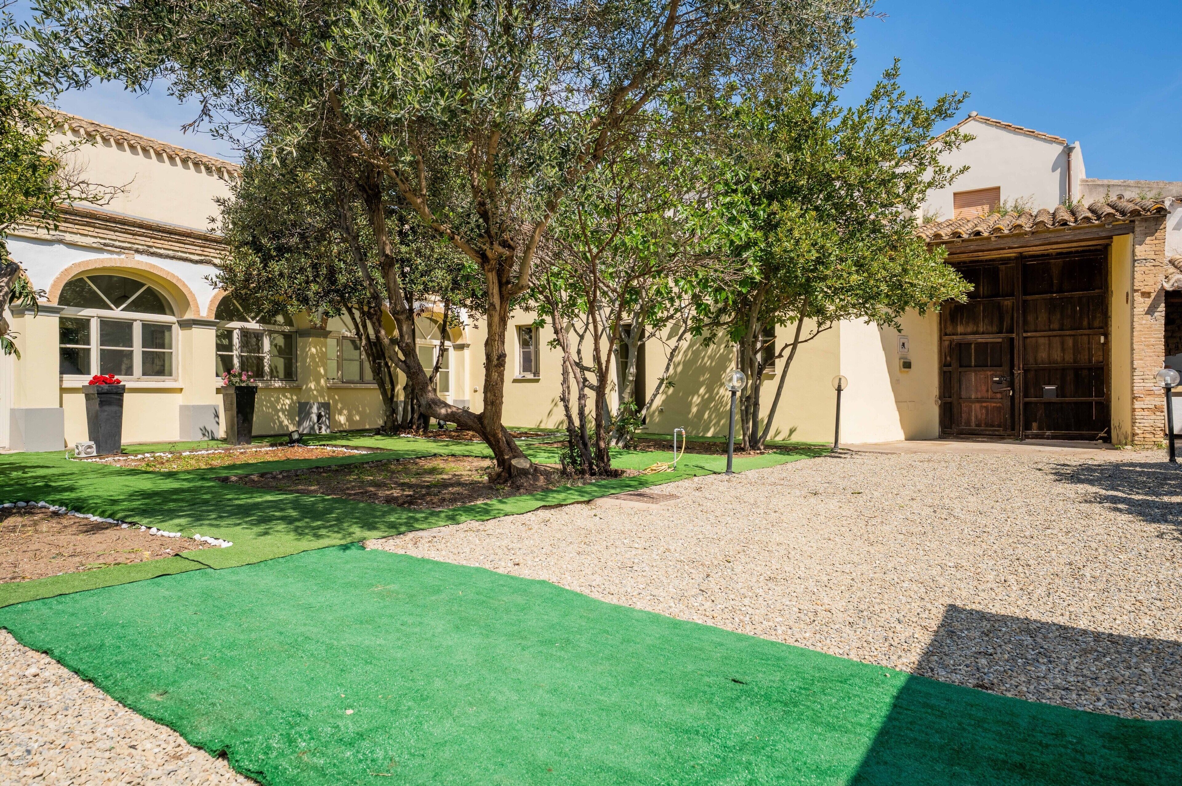 Un cortile con vialetto in ghiaia, prato sintetico verde e alberi.