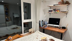 Ein Schlafzimmer mit Bett, Schreibtisch und Computer, sowie einem Fenster.