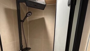Ein kleiner Duschbereich mit gefliesten Wänden, einer Handbrause und Ablagefläche.