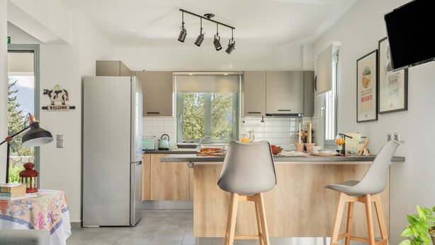 Cocina moderna con una isla central, taburetes de bar, un refrigerador y un comedor con mesa y sillas.