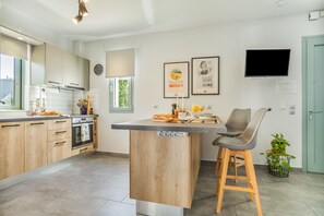 Une cuisine moderne avec des armoires en bois, un four encastré, un grand îlot central doté de tabourets de bar et un téléviseur à écran plat fixé au mur.