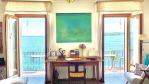 Quarto com mesa de madeira, duas cadeiras, um quadro verde e vista para o mar.