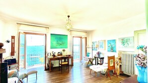 Um quarto amplo com piso de madeira, área de refeições e vista para o mar por grandes janelas.
