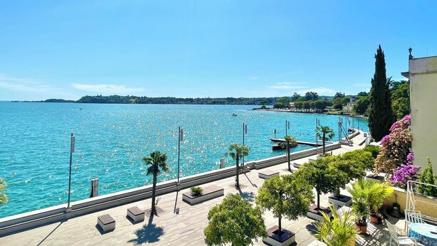 Um calçadão à beira-mar com vista ampla para o oceano, um cais e uma fileira de vasos de plantas com áreas de estar.