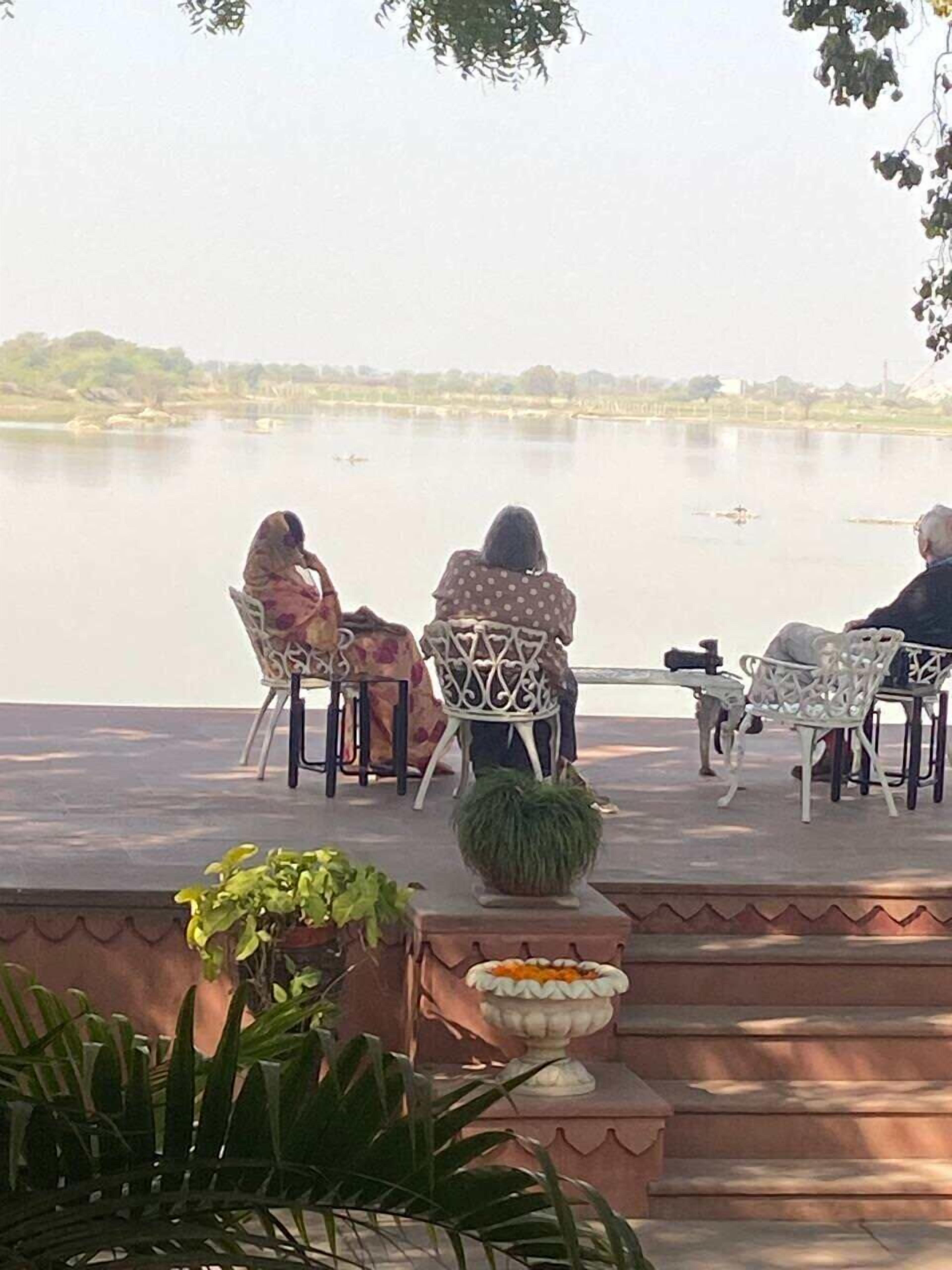 A terrace with three chairs and a table, overlooking a calm body of water.