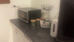 Una cucina con forno a microonde, macchina del caffè e televisore su un piano di lavoro in marmo.
