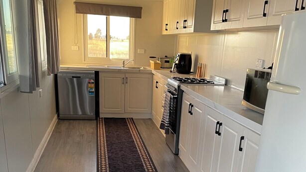 A modern kitchen with white cabinets, stainless steel appliances, and a patterned rug. - Cabin and horse paddock for rent (Bective)