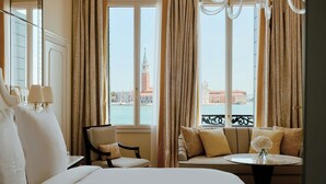 A hotel room with a bed, a chair, a sofa, a table, and a view of a cityscape through large windows. - Danieli, A Four Seasons Hotel, Venice (Venice)