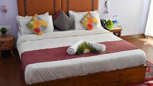 A neatly made bed with a red blanket, a wooden headboard, and colorful floral pillows. - Hotel Rosh Villa (Manali)