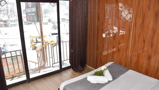 A hotel room with a bed, a window with a view of the outside, and a wooden wall. - Hotel Rosh Villa (Manali)