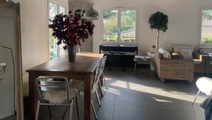 Ett rymligt vardagsrum med ett matbord, stolar, ett piano och en mysig sittgrupp med kuddar.