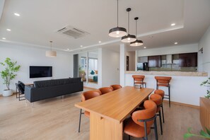 Un salon moderne avec un canapé, un téléviseur et un coin repas comprenant des chaises et une table en bois.