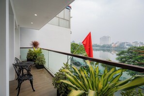 Un balcon avec une table et des chaises, des plantes en pot et une vue sur le paysage urbain et une étendue d’eau.