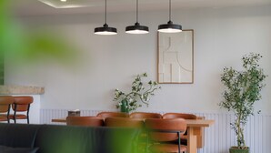 Ein Essbereich mit Holztisch und Stühlen, Pendelleuchten, einem Blumentopf und einem gerahmten Kunstwerk an der Wand.