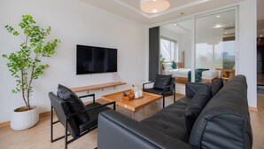 Ein modernes Wohnzimmer mit einer Couch, Sesseln, einem Couchtisch, einem Fernseher und einer Topfpflanze.