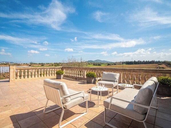 Une terrasse extérieure avec deux chaises blanches rembourrées, une petite table ronde et un pot de fleurs.